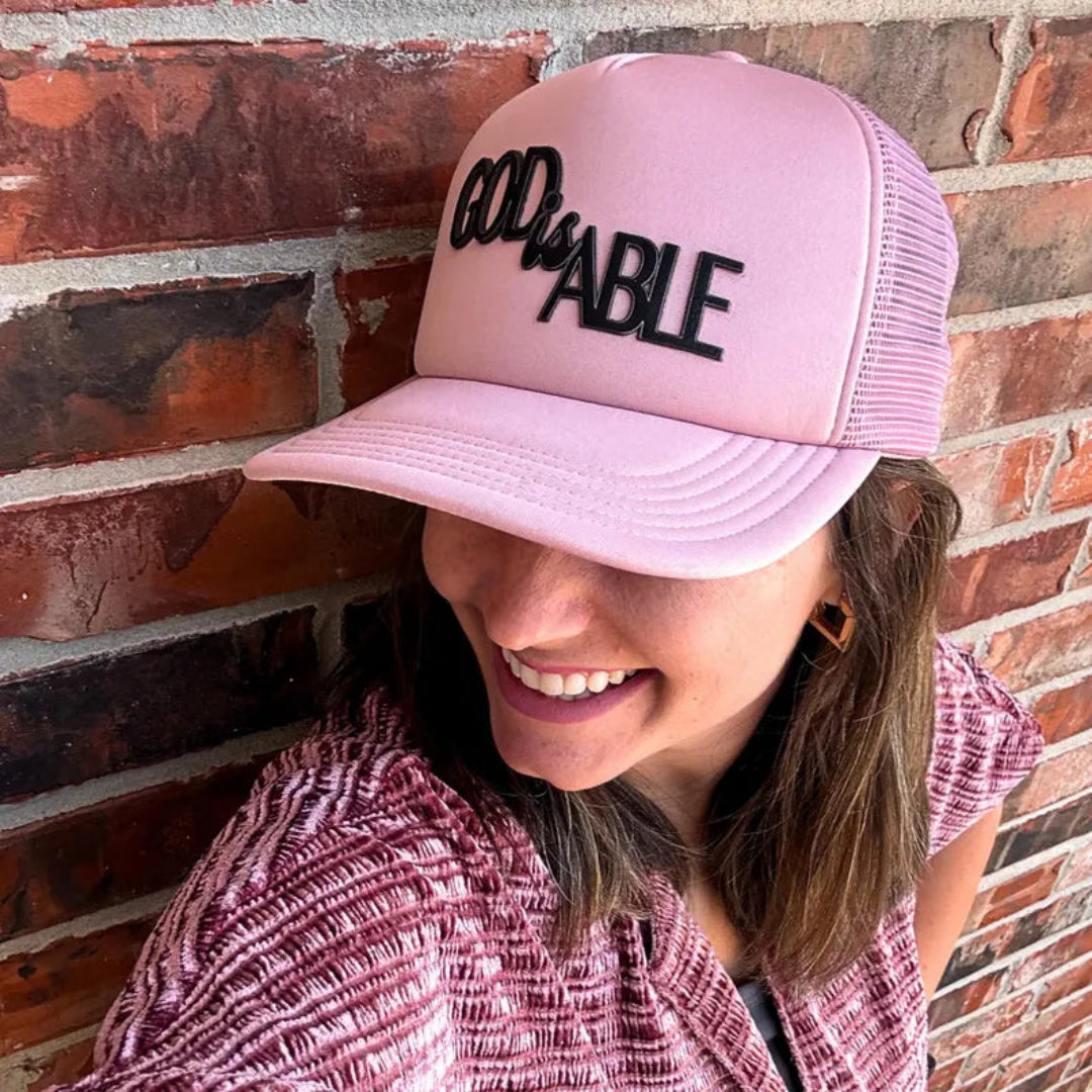 Woman wearing a pink GOD is ABLE trucker hat