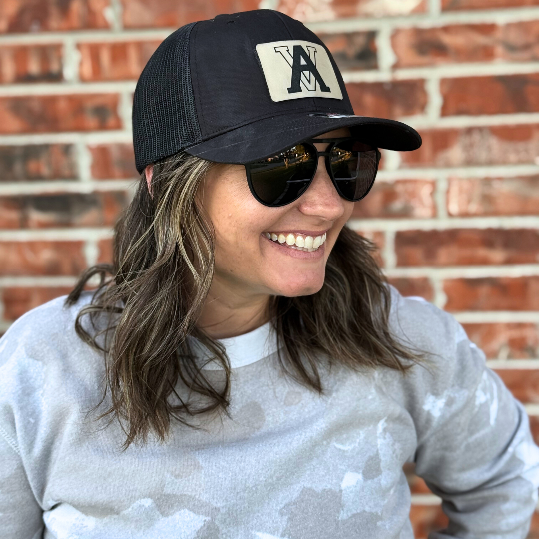 Woman wearing a black trucker hat with an engraved initial patch