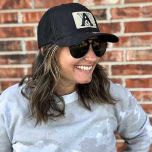 Woman wearing a black trucker hat with an engraved initial patch