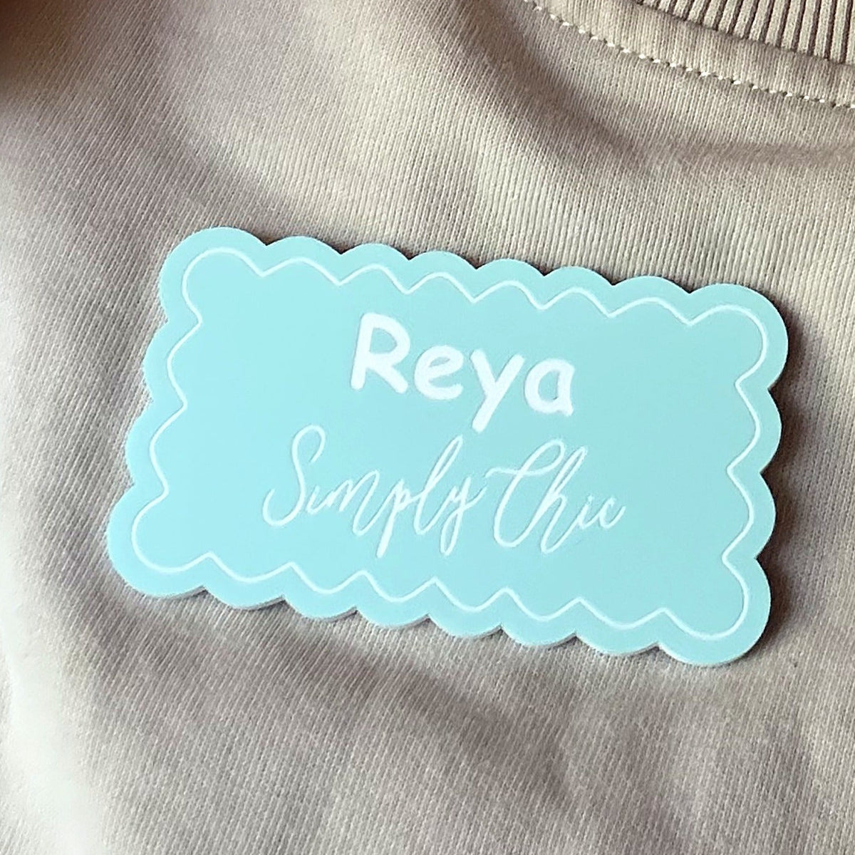 Mint scalloped name badge worn on a sweatshirt