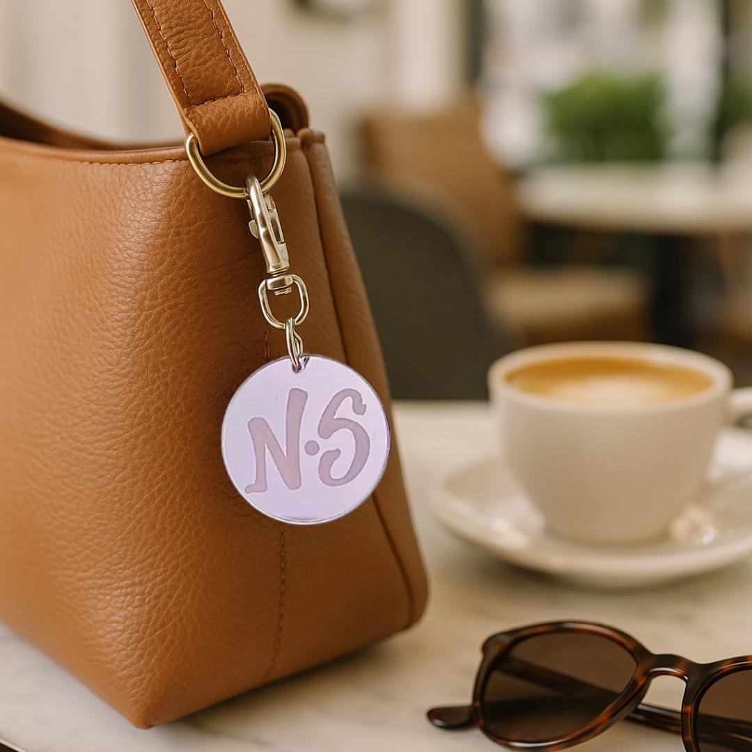 Pink mirror acrylic keychain with an NS logo on a handbag