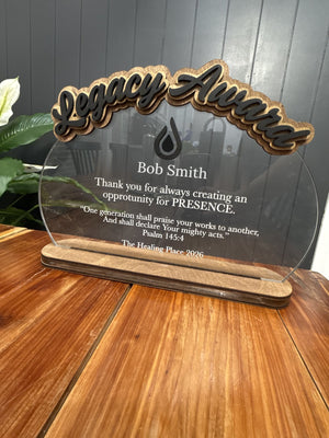 Clear acrylic award with raised script Legacy Award title in wood and black, white text and a wood base
