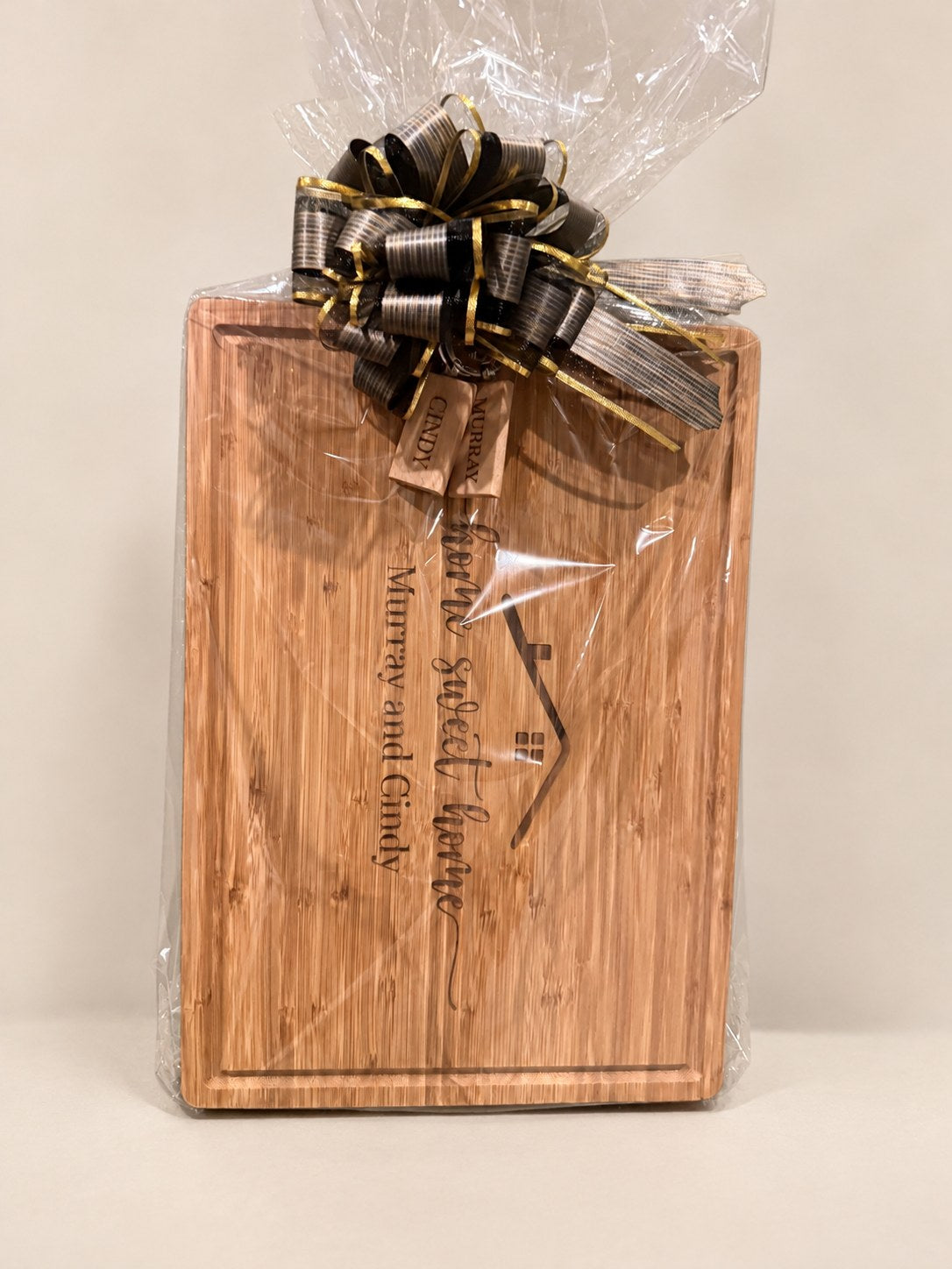 Bamboo cutting board engraved with Home Sweet Home, a house roofline and two names, gift wrapped with a bow and two engraved keychains