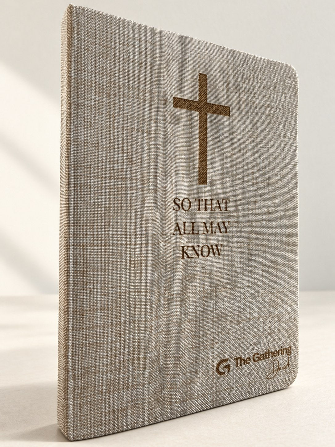 Linen-cover hardcover journal standing on a table, laser engraved with a cross, So That All May Know, and a church logo