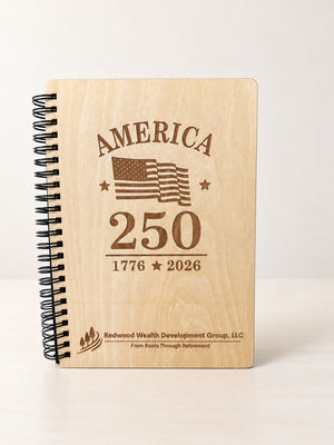 Wood spiral notebook with a black spiral standing on a table, laser engraved with America 250, a flag and a company logo