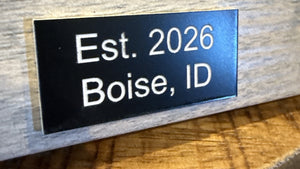 Black acrylic plate engraved with white text, Est. 2026 Boise, ID, on the bottom of a picture frame